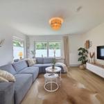 Wohnzimmer mit grauem Sofa, Holzboden und Fernseher an der Wand.
