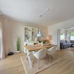 Essbereich mit Holztisch und Stühlen. Wohnzimmer mit Sofa und Fenstern.