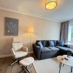 Ein Wohnzimmer mit grauem Sofa, beigefarbenem Sessel und Holzboden. An der Wand hängt ein Bild.