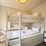 Zimmer mit Doppelstockbett, Schreibtisch und Stuhl. Beleuchtung und kleine Regale.
