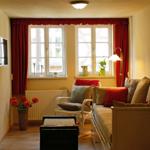 Wohnzimmer mit Sofa, Sessel, Fenstern, Vorhängen und Fernseher an der Wand.