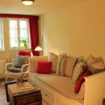 Ein Wohnzimmer mit Sofa, Sessel, Fenstern und Pflanzen.