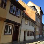 Straße mit historischen Häusern und roten Ziegeldächern unter blauem Himmel.