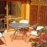 Terrasse mit runden Tisch und drei Stühlen, umgeben von Blumen und einem Holzzaun.