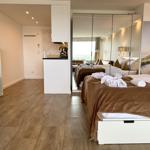 Schlafzimmer mit Bett, Spiegelschrank und Küchenbereich im Hintergrund.