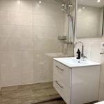 Badezimmer mit Dusche, Waschbecken und Spiegel. Fliesenwand und Holzboden.