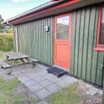 Grünes Holzhaus mit roter Tür, Picknicktisch und Gartenbereich.