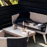 Außenbereich mit wicker Sofa, Tisch und Stühlen. Schwarze Decken und Getränke darauf.
