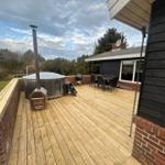 Terrasse mit Holzdecke, Whirlpool, Grill und Sitzgruppe. Blick auf Wald und Himmel.