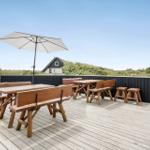 Terrasse mit Holztischen, Bänken und Sonnenschirm. Blick auf grüne Landschaft und Haus.