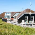 Haus mit Strohdach, Terrasse und Garten. Sonnenschirm, Tische und Liegestühle.