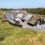 Haus mit Strohdach und Holzterrasse, Gartenmöbel und Blick auf Grünland.
