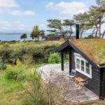 Hütte mit Grasdach und Holzterrasse, Blick auf Wasser und Bäume.