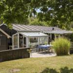 Haus mit Terrasse, Tisch und Stühlen unter Bäumen. Grünfläche und Schutzdach.