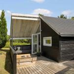 Schwarzes Holzhaus mit Terrasse, Sitzbank und Grill unter Dach.
