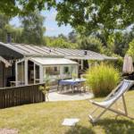 Haus mit Terrasse, Garten und Liegestuhl unter Bäumen.