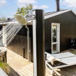 Außen-Dusche auf Holzterrasse neben Holzhaus mit Liegen und Grillplatz.