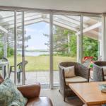 Wohnbereich mit Blick auf einen Garten und See. Rattanstühle, Holztisch und Ledersofa.