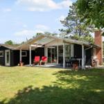 Ein Haus mit Terrasse, roten Stühlen und grünem Garten. Holzhaus mit Kamin und Glasfront.