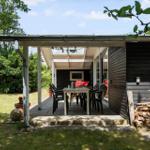 Terrasse mit Tisch und Stühlen, Holzstapel und grünem Gartenbereich.