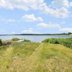 Grasfläche mit Blick auf einen See unter blauem Himmel mit weißen Wolken.