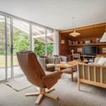 Wohnzimmer mit braunem Ledersessel, Holzmöbel und Glasfront zur Terrasse.