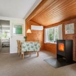 Raum mit Esstisch, Kamin und Blick auf Grün. Holzdecke und Wand. Schlafzimmer im Hintergrund.