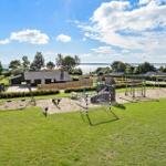 Großer Spielplatz mit Sandkasten, Schaukel und Klettergerüst vor Ferienhaus mit Blick auf Wasser.