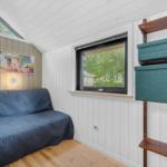 Ein Raum mit Sofa, Fenster und Regal. Holzfußboden und weiße Wände.