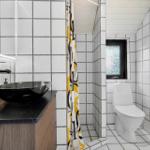 Badezimmer mit Waschbecken, Toilette und Dusche. Fliesenwand und schwarzer Waschtisch.