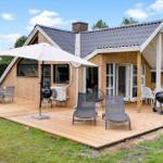 Holzhaus mit Terrasse, Grill und Sitzgelegenheiten im Freien.