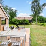 Terrasse mit Tisch, Stühlen und Sonnenschirm neben Holzhäuser. Grasfläche und Bäume im Hintergrund.