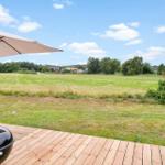 Terrasse mit Sonnenschirm und Grill, Blick auf grünes Feld und Bäume.