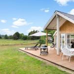 Terrasse mit Tisch, Stühlen, Grill und Liegen. Grünfläche und Wald im Hintergrund.