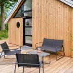 Terrasse mit Sitzgruppe und Pflanzen vor einem Holzhaus mit Glasfront.