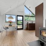 Raum mit Esstisch, Kamin und großem Fenster. Holzboden und weiße Wände.