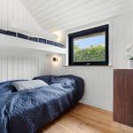 Schlafzimmer mit Doppelbett und Hochbett, Holzboden und Fenster mit Blick auf Grün.