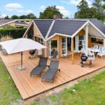 Holzhaus mit Terrasse, Sonnenliegen, Grill und Sitzgruppe unter einem Vordach.
