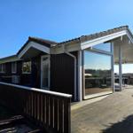 Moderne Villa mit Holzterrasse und großem Glasbereich. Personen sind im Außenbereich sichtbar.