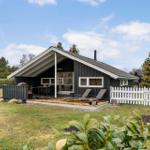 Ein Haus mit Holzterrasse, Liegestühlen und weißem Zaun auf grünem Grund.
