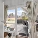 Durchgehende Glasfront öffnet sich auf eine Terrasse mit Tisch und Stühlen. Vor dem Haus liegt ein Garten.