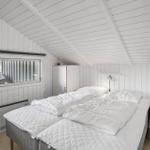 Schlafzimmer mit Doppelbett, weißen Wänden und Dachschrägen. Fenster, Schrank und Stuhl sichtbar.