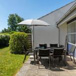 Terrasse mit Tisch, Stühlen und Sonnenschirm. Grasfläche und Hecke im Hintergrund.