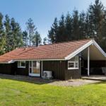 Holzhütte mit Terrasse, Garten und Wald im Hintergrund.