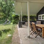 Terrasse mit Holztisch, Stühlen und Liegestühlen im Garten. Schwarze Hauswand mit Fenster.