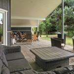 Terrasse mit Sitzgruppe, Tisch und Grillbereich unter Dach.