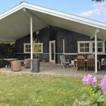 Haus mit überdachter Terrasse, Gartenmöbeln und Blumen im Vordergrund.