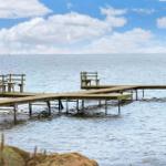Holzsteg mit Sitzgelegenheiten am Wasser. Blick auf ruhiges Meer unter blauem Himmel.