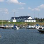 Hafen mit Booten und weißem Gebäude im Hintergrund unter blauem Himmel.