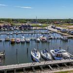 Hafen mit Booten und Holzstegen. Im Hintergrund sind Häuser und Grünflächen.